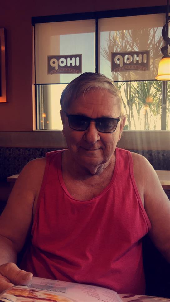 An elderly man wearing a red tank top and sunglasses sits indoors, ready for a meal.