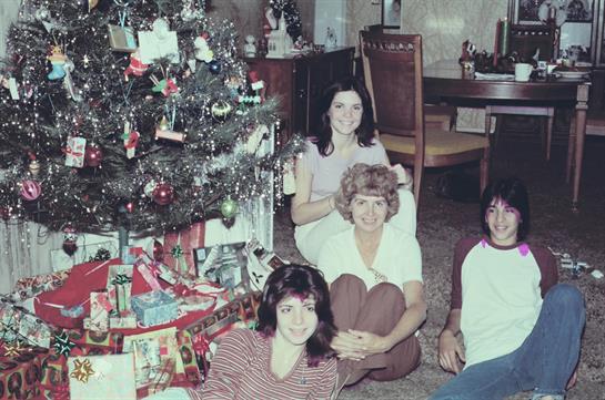 Four individuals celebrate Christmas together next to a beautifully decorated tree and gifts.