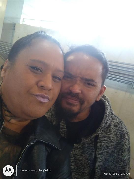 Two individuals are smiling closely together, enjoying a moment indoors in bright light.