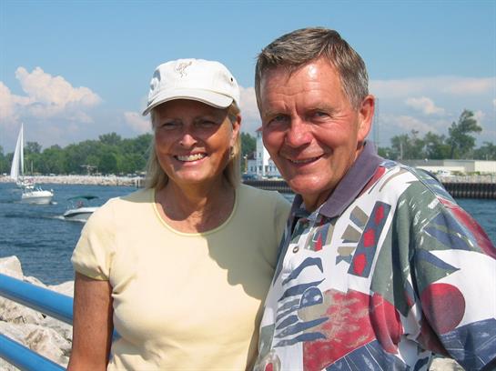 A cheerful couple smiles together near the waterfront on a bright, sunny day.
