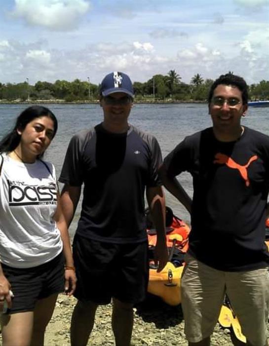 Three friends stand by the water, ready to embark on a kayaking adventure under a clear sky.