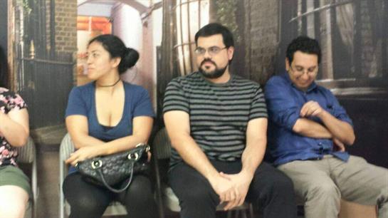 Four individuals sit quietly in a waiting area, each engaged in their own thoughts or conversations.