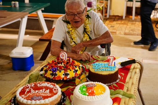 Elderly person enjoys a celebration surrounded by decorated birthday cakes and family.