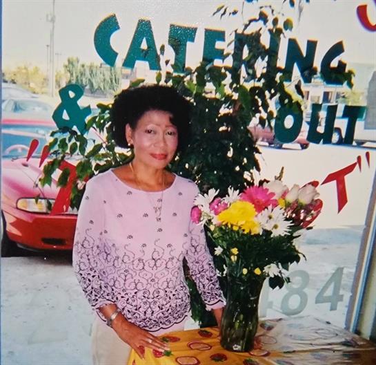 A woman stands beside a vase of flowers in a catering establishment, smiling warmly.