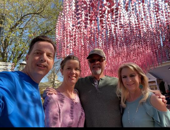 Four friends pose together under vibrant pink decor during a sunny spring day.