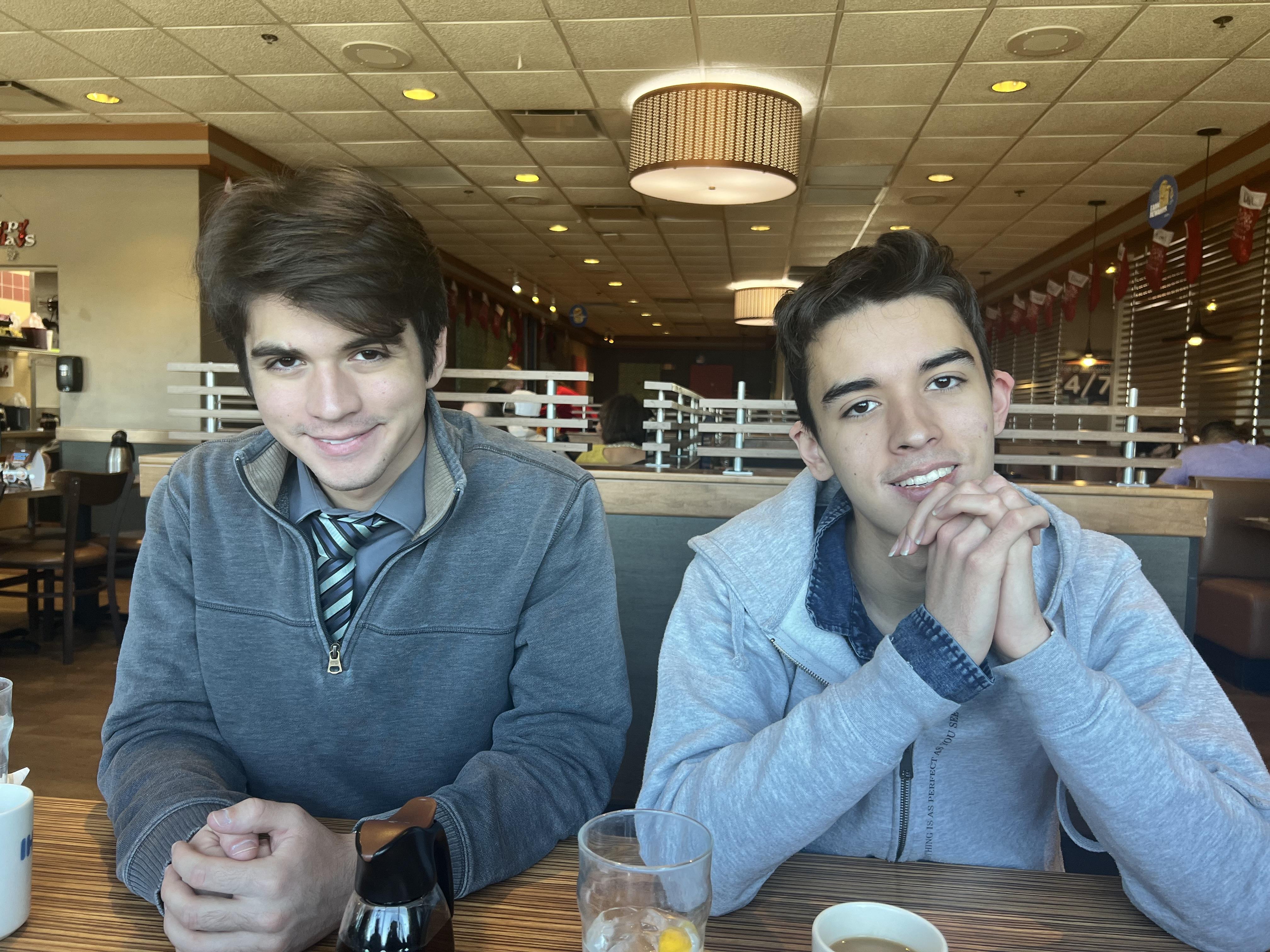 Two young friends sit together at a restaurant table, smiling and chatting over drinks.