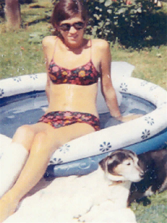 A woman in a garment sitting in a small pool with a dog