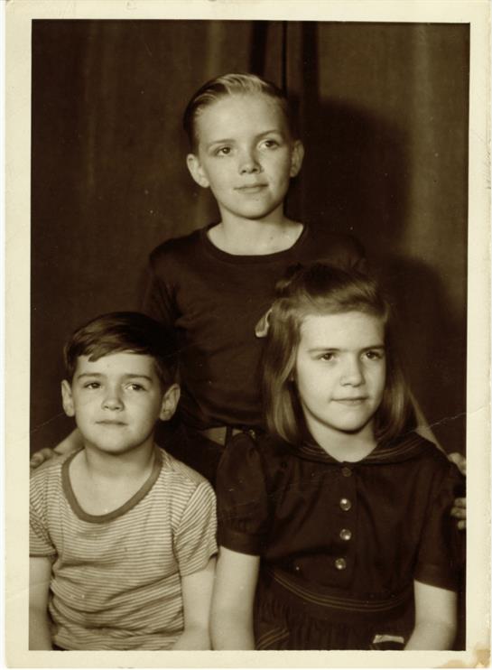 Three children dressed in vintage attire are posing together, showcasing their serious expressions.
