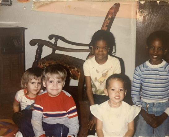 Five children are gathered in a cozy indoor space, laughing and playing together.