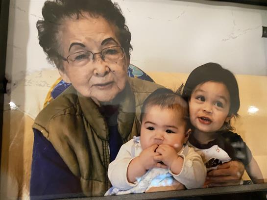 A grandmother smiles contently while embracing two playful young children in a cozy environment.