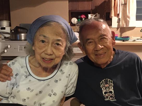 An elderly couple smiles lovingly together in their kitchen, cherishing their time.