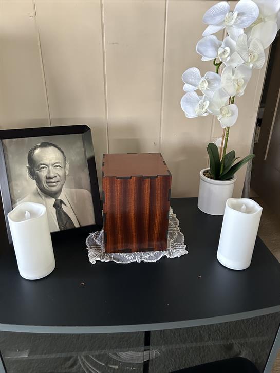 A side table displays a wooden box, two candles, a floral arrangement, and a portrait of a man.