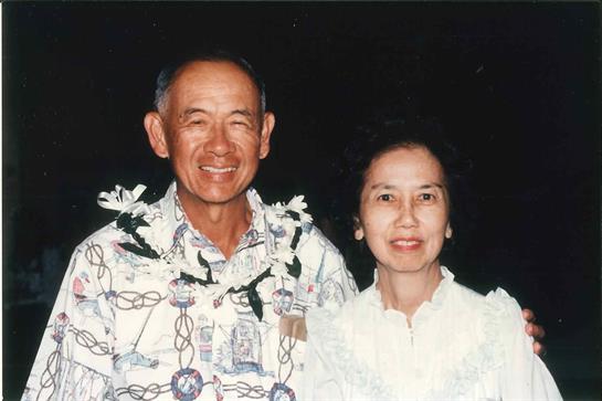 Elderly couple enjoys a festive Hawaiian celebration while wearing leis and traditional clothing.