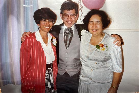 Three friends pose joyfully in a festive indoor setting, celebrating a memorable event.