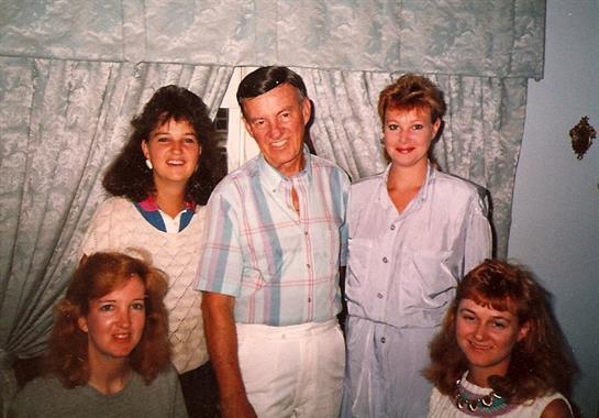 Five relatives share smiles and laughter in a welcoming living area filled with light.
