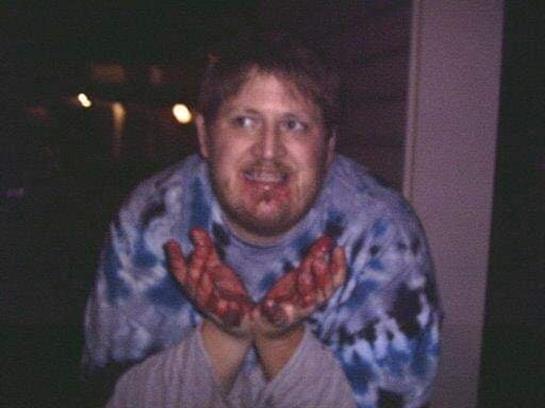 Happy individual with red-stained hands in a colorful tie-dye shirt outdoors at night.
