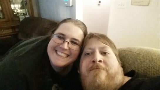 A happy couple smiles together on the couch, enjoying a cozy moment.