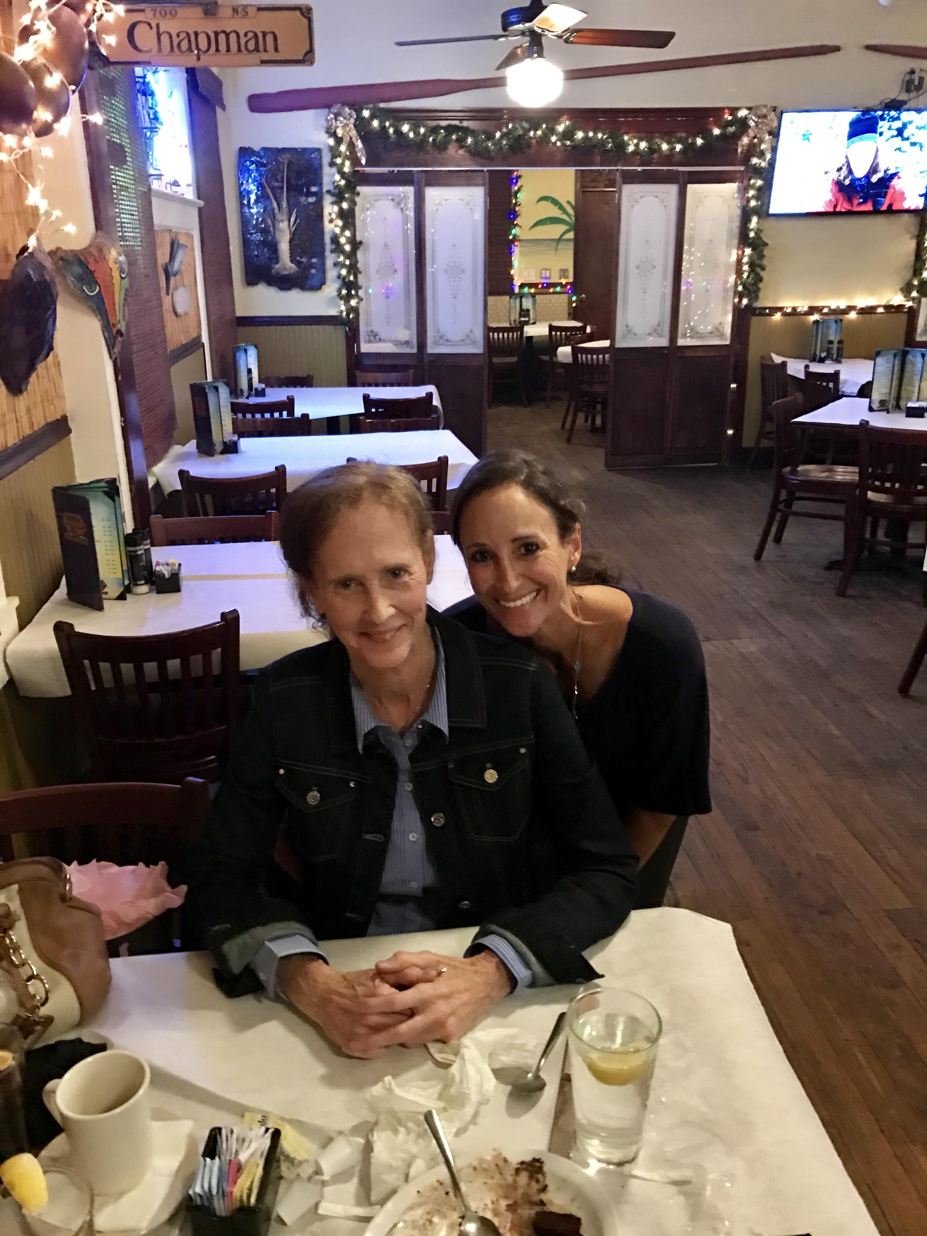 Two women sit at a table sharing dessert in a warm restaurant atmosphere during the evening.
