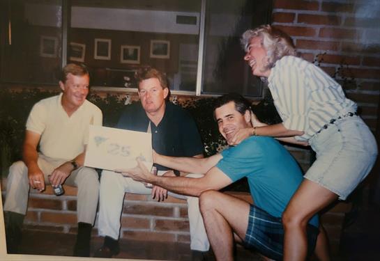 Four friends gather in a relaxed environment, sharing a lighthearted moment with a gift.