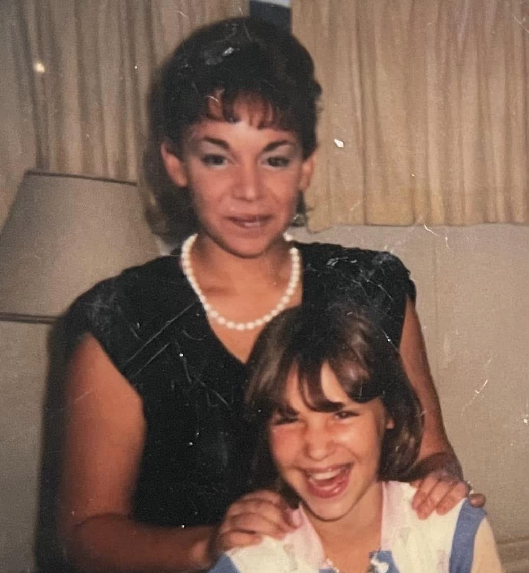 A woman and girl are sharing a joyful moment in a warmly lit indoor space.
