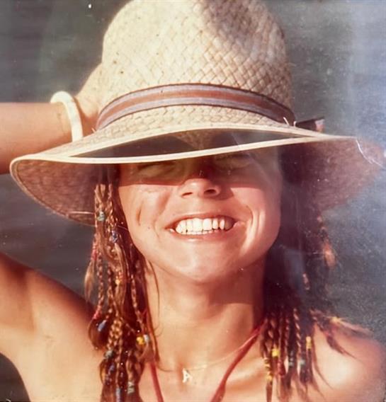 A joyful woman with braided hair, wearing a sun hat, is enjoying a warm summer day at the beach.