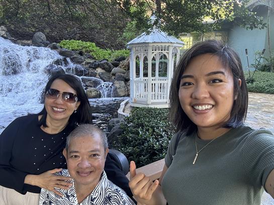 Friends relax and smile by a stunning waterfall in a scenic garden on a sunny day.
