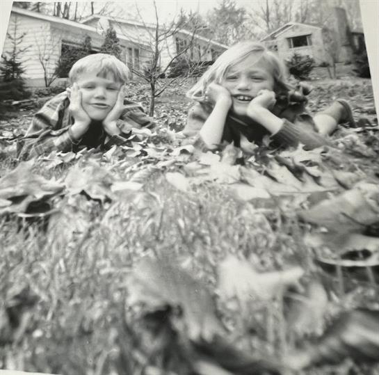Two children are enjoying their time in a backyard filled with autumn leaves.