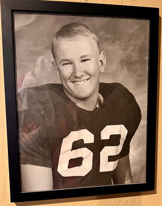 A smiling young man in a 1960s football uniform exudes pride and energy.