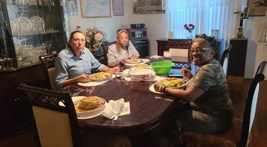 Three friends enjoy dinner together, sitting at a beautifully set dining table filled with food.