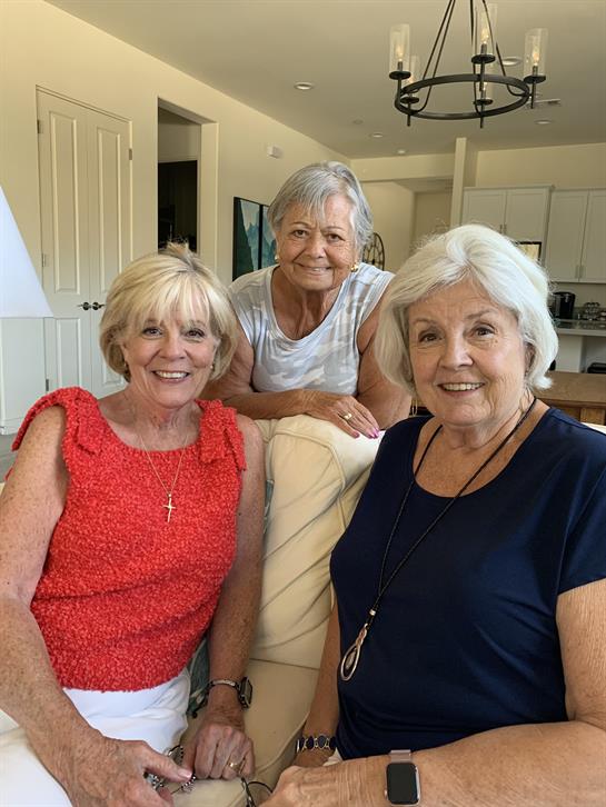 Three women share laughter and warmth in a bright living room, showcasing their friendship.