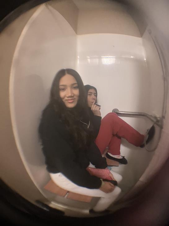 Friends share a moment in a restroom, smiling and relaxed while seated in casual attire.