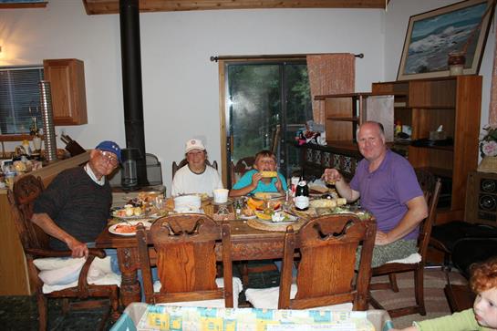 Friends and family share a meal around a wooden dining table in a warm home setting.
