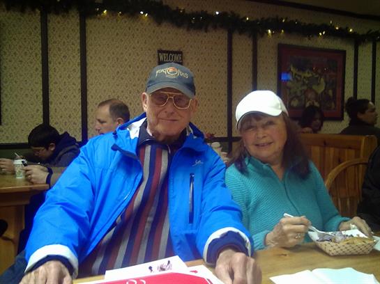 An elderly couple smiles while sharing dessert in a warm, inviting cafe during winter.