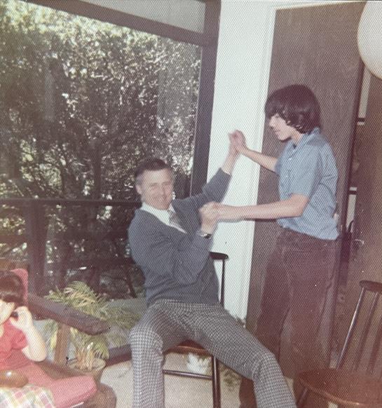 Two family members engage in playful wrestling while a child observes with curiosity.