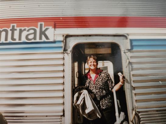 A joyful traveler greets the day as she steps off the train with bags in hand.