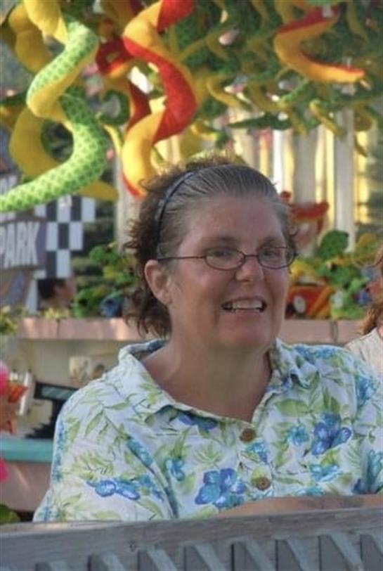 A joyful woman poses at a carnival with vibrant decorations surrounding her.
