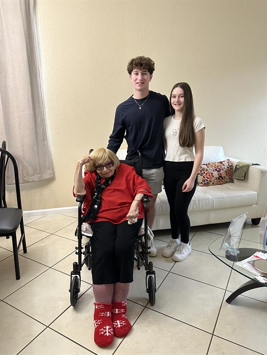 Two young adults stand beside an elderly woman in a wheelchair, celebrating together.