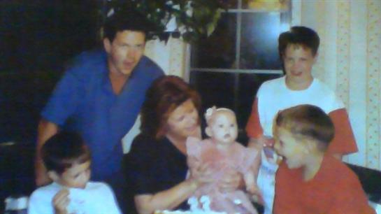 A family gathers around a table, celebrating a young girl's special occasion with laughter.