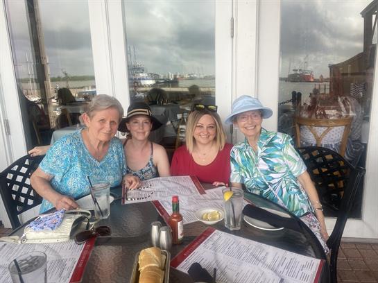 Four women gather at a table by the water, sharing laughter and conversation while dining.