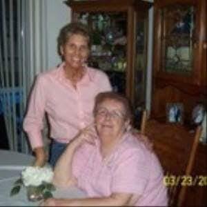 Two women share a joyful moment at a dinner table with a floral centerpiece at home.