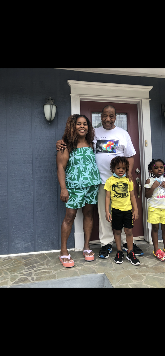 Family posed happily on a porch outside a blue house on a summer afternoon.