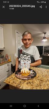 A man stands proudly next to a decorated cake on a kitchen countertop, enjoying the celebration.