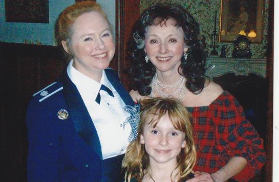 Three women, dressed in warm outfits, share smiles in a cozy room decorated for winter festivities.