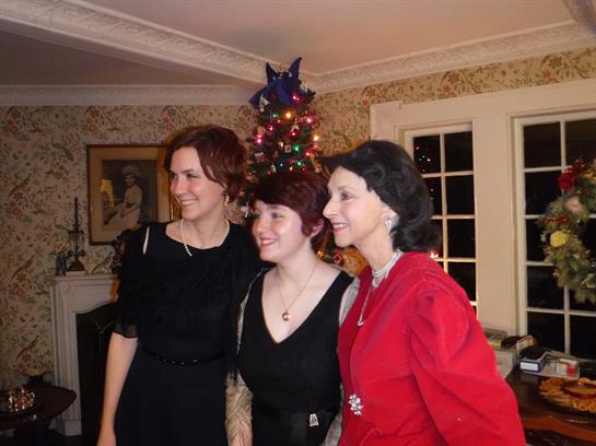 Three women pose joyfully together in a festively decorated living room during a holiday gathering.