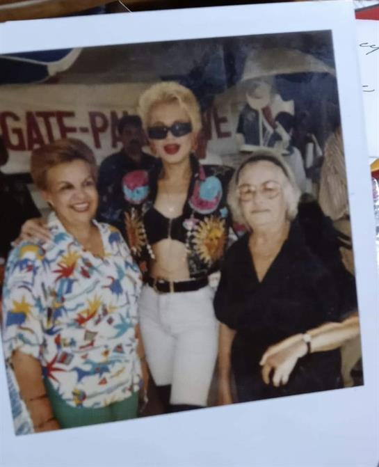 Three women pose together with unique fashion choices at a lively event celebrating culture.