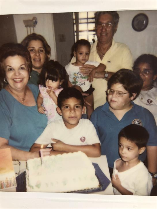 A family celebrates a birthday with cake in a joyful kitchen gathering.