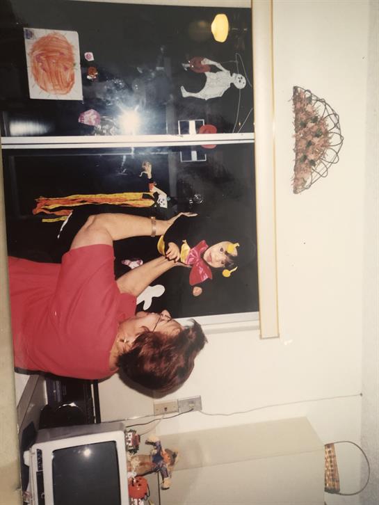 A woman plays with a puppet while surrounded by kitchen decor, creating a lighthearted atmosphere.