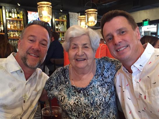 Two men happily pose with an elderly woman at a lively restaurant, savoring family time.