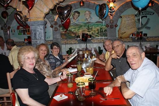 A group of friends enjoys a happy occasion at a lively dining venue, surrounded by decorations.