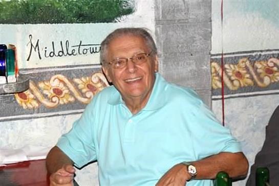 A joyful elderly man is seated at a table with friends, sharing laughter and stories.